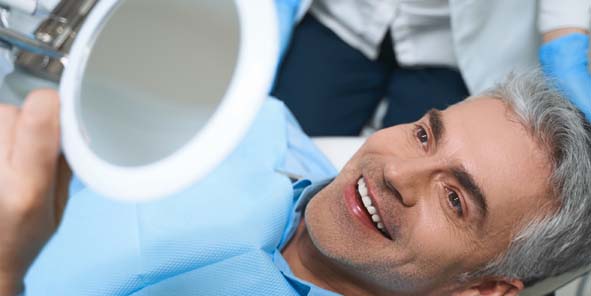 Patient blickt in Spiegel und freut sich über sein Zahnimplantat - Ablauf der Behandlung abgeschlossen.