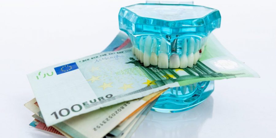 Gebiss-Modell und Geldscheine symbolisieren die Kosten für Zahnimplantate.